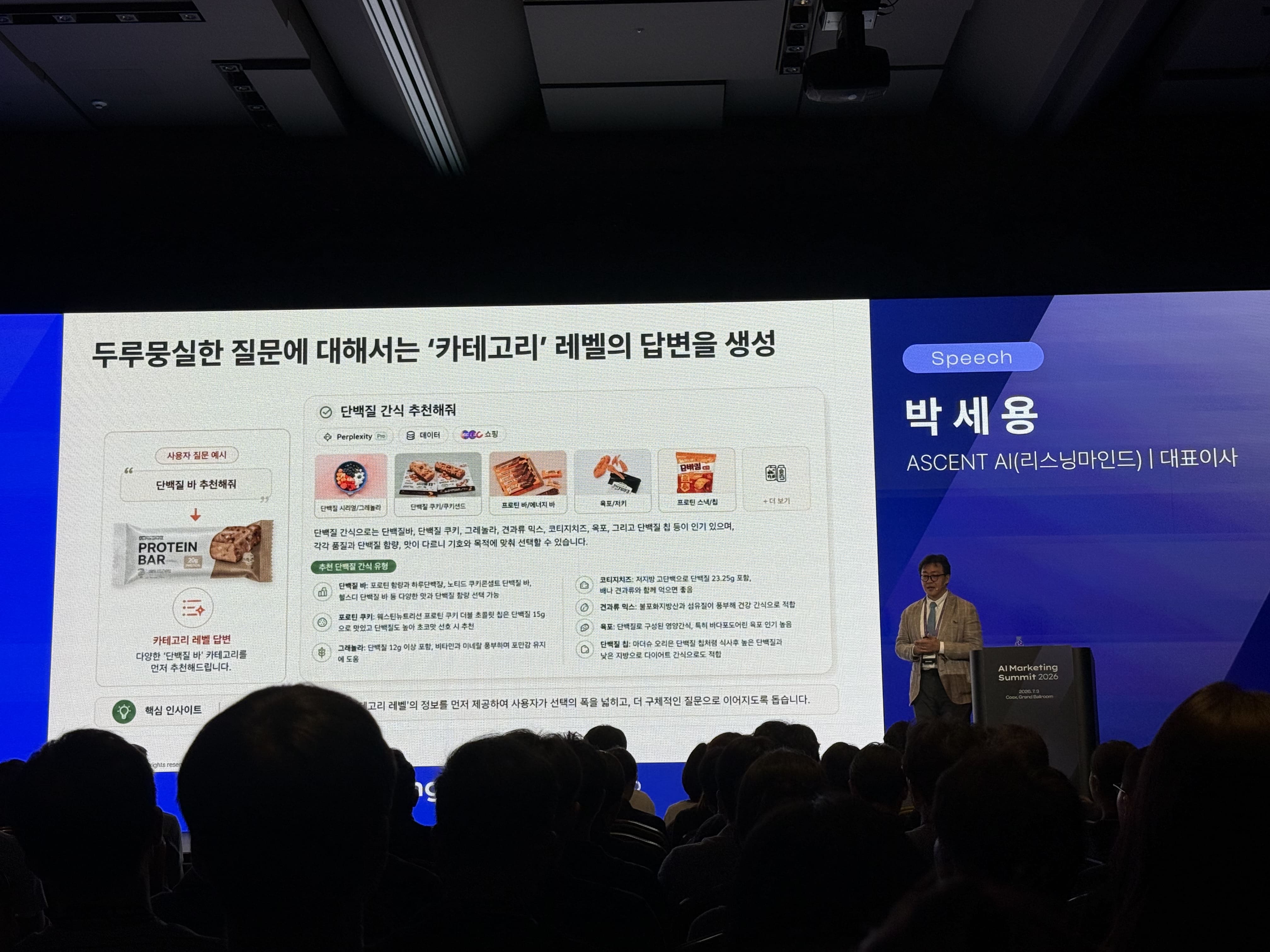 서울메타위크 AI Marketing Summit 2026 박세용 대표 세션. 두루뭉술한 질문에 대해서는 카테고리 레벨의 답변을 생성한다는 슬라이드가 보인다. 사용자가 단백질 바 추천을 요청하면 AI는 단백질바, 단백질 쿠키, 그래놀라, 견과류 믹스, 프로틴 스낵 등 카테고리 수준의 후보를 먼저 추천한다.