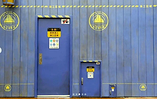 파란색 공사장 가벽에 문틀과 손잡이가 달린 큰 문, 그보다 작은 문, 아주 작은 문이 나란히 붙어 있는 모습